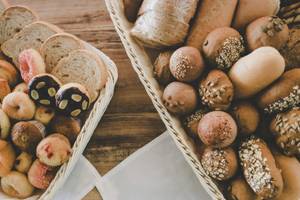 Zwei Körbe mit verschiedenen Gebäckstücken und Broten auf einem braunen Tisch