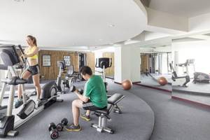 Fitnessstudio im Beyond Resort Krabi mit einer Frau auf dem Laufband und einem Mann, der Gewichte hebt.