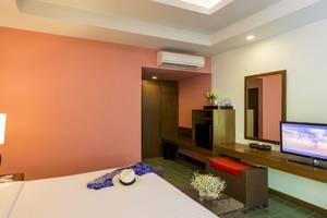 Innenansicht eines Hotelzimmers im Beyond Resort Krabi mit rosa Wand, Fernseher, Tisch, Lampe und Hut.