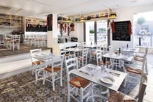 Innenansicht des Restaurants im Louis St. Elias Resort & Waterpark mit weißen Tischen und Stühlen, gefliesten Böden und einer Tafel mit Speisen.