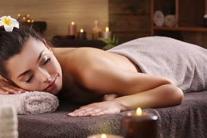 Eine Frau genießt eine Massagebehandlung im Ellaidhoo Maldives Spa mit Kerzen und Blütenblättern.