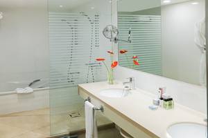 Badezimmer im H10 Gran Tinerfe Hotel mit Badewanne, Waschbecken und Spiegel.