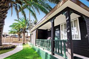 Außenansicht des Oasis Belorizonte Ferienhauses mit grüner Veranda und Palmen im Hintergrund.