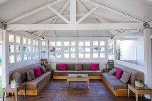 Innenbereich des Oasis Belorizonte Hotels mit weißen Wänden und Holzböden, mehrere Sofas mit Kissen und Tischen.