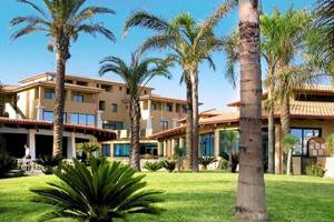 Außenansicht des TH Le Castella - Baia degli Dei Village Hotels mit Gebäuden, Palmen und grüner Rasenfläche.