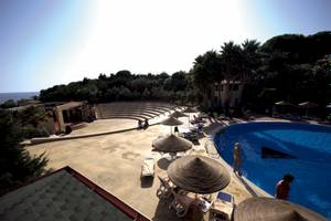 Oberansicht des TH Le Castella - Baia degli Dei Village mit Pool, Liegestühlen und Sonnenschirmen.