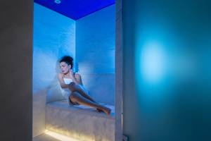Eine Frau sitzt entspannt in einer blau beleuchteten Sauna im Silva Beach Hotel.