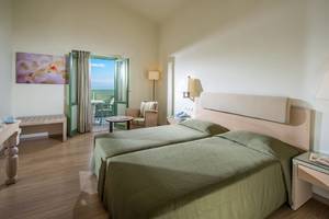 Zimmer im Silva Beach Hotel mit zwei grünen Betten, einem Balkon, einem Tisch und einem Stuhl.