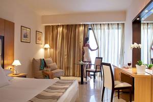 Innenansicht eines Hotelzimmers im Lindos Bay Hotel mit einer Frau, die einen Vorhang öffnet.
