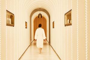 Eine Frau in einem weißen Bademantel geht durch den Eingang des Spas im Raffles The Palm Dubai.