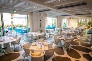 Innenansicht des Restaurants Raffles The Palm Dubai mit weißen Tischen und Stühlen und einem braun-weißen Bodenmuster.