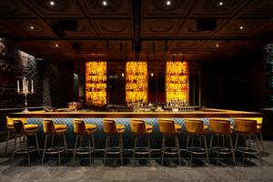 Bar-Szene im Raffles The Palm Dubai mit gelben Barhockern und einer Theke voller alkoholischer Getränke.