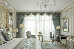Innenansicht der Suite im Raffles The Palm Dubai mit großem Bett, Schreibtisch und Kristallkronleuchter.