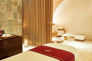 Spa-Behandlungsraum im Raffles The Palm Dubai mit Holzelementen, Sitzgelegenheiten und einem Tisch mit Wellnessprodukten.