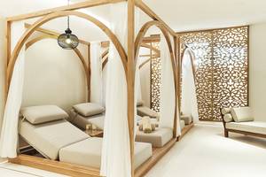 Spa-Lounge-Bereich im Raffles The Palm Dubai mit hölzernen Liegen, weißen Vorhängen und einer goldenen Wand.