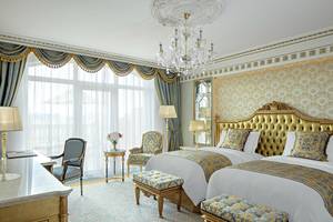 Schlafzimmer im Raffles The Palm Dubai mit zwei Betten, goldenen Kopfteilen, Kristallkronleuchter und eleganter Einrichtung.