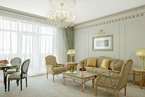 Wohnzimmer im Raffles The Palm Dubai Hotel mit Kristallkronleuchter, goldenen Möbeln und Früchtekorb auf dem Tisch.