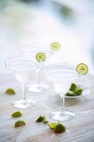 Drei Cocktails mit Limettenscheiben auf einem Holztisch.