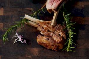 Gegrilltes Lamm mit Rosmarin und Blumen auf einem Holztisch