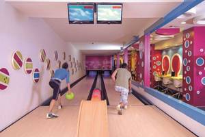 Zwei Leute bowlen in einer Halle mit bunten Wänden und Bowlingbahnen.