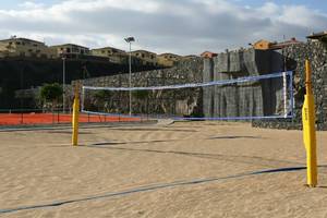 Ein Volleyballnetz auf einem Sandstrand mit einer Steinmauer im Hintergrund.
