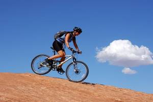 Frau mit Fahrrad auf einem Berg, im Himmel ist eine Wolke sichtbar