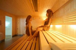 Zwei Frauen in einer Sauna mit Holzwänden und warmem Licht.