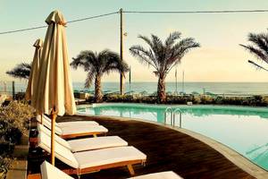 Außenpool des Aegean Pearl Hotels mit Sonnenliegen und Palmen am Strand