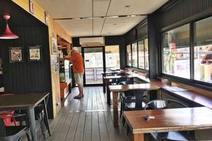 Innenansicht des Restaurants im Pavillon Samui Villas & Resort, mit einem Mann, der an einer Bar steht, und leeren Tischen und Stühlen.