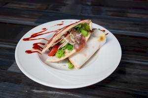 Ein Teller mit einem Sandwich, das mit Salat, Tomaten und Schinken gefüllt ist, und eine rote Sauce.