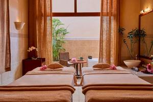 Spa-Behandlungsraum im Jaz Mirabel Beach Hotel mit zwei Massageliegen, einem Tisch und einem Fenster.