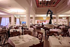 Esszimmer im Bahia Principe Luxury Esmeralda Hotel mit Tisch, Stühlen, Statue und Kronleuchtern.
