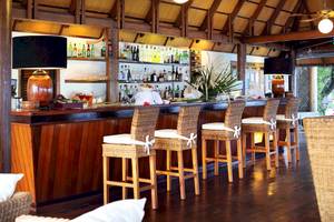 Barbereich im Gangehi Island Resort mit Holzstühlen, Theken und gefüllten Regalen.