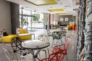 Lobbybereich des Gladiola Star Hotels mit bunten Stühlen und Tischen, gelben Sofas und einer Steinmauer.