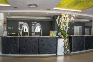 Innenansicht der Rezeption im Gladiola Star Hotel mit schwarzem gepolsterten Tresen, weißen Blumen und moderner Gestaltung.