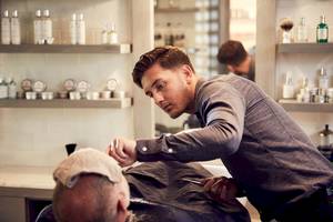 Friseur in einem Salon, der einen älteren Mann rasiert