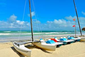Mehrere Boote, darunter ein Katamaran, am Strand des Iberostar Tainos Hotels.