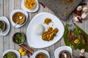 Ein Gericht mit Curry und Reis auf einem Holztisch, umgeben von Gewürzen und Zutaten.