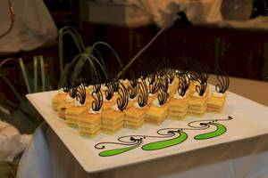 Foto von einem weißen Teller mit mehreren Stücken Kuchen gefüllt mit einer gelben Creme und schwarzen Dekorationen.