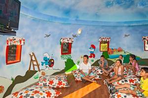 Kinderzimmer mit Schlumpfisch-Wandmalerei und Kindern, die auf Kissen sitzen.