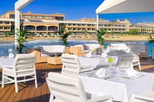 Gedeckter Tisch auf einer Terrasse am Strand vor dem Secrets Bahia Real Resort & Spa Hotel.