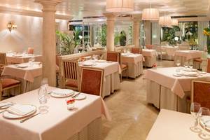Innenansicht des Restaurants des Secrets Bahia Real Resort & Spa mit gedeckten Tischen, eleganten Stühlen und beleuchteten Kronleuchtern.