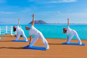 Drei Personen machen Yoga auf einer Plattform am Pool im Gewässer