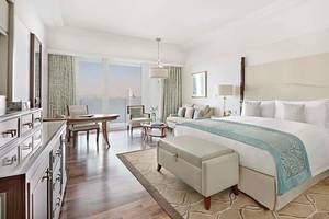 Innenansicht einer Suite im Waldorf Astoria Dubai Palm Jumeirah mit großem Bett, Schreibtisch und Blick auf das Meer.