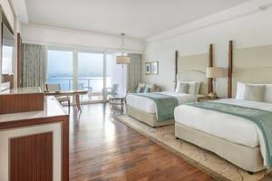 Innenansicht einer Suite im Waldorf Astoria Dubai Palm Jumeirah mit zwei Betten, Schreibtisch und Meerblick.
