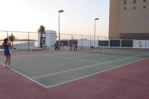 Tennisplatz im Waldorf Astoria Dubai Palm Jumeirah mit Spielern und Arbeitern im Hintergrund.