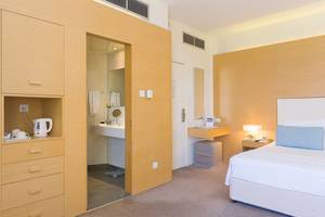 Innenansicht des Schlafzimmers im Capo Bay Hotel mit einem Bett, Nachttisch, Lampe und offenem Badezimmer.