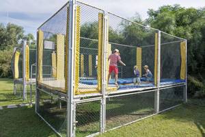 Ein Trampolin-Spielplatz im Freien, umzäunt mit Netzen, mit Kindern, die spielen.
