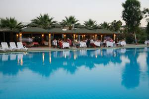Gäste sitzen bei Tischen neben dem Swimmingpool im Palm Wings Ephesus Beach Resort.