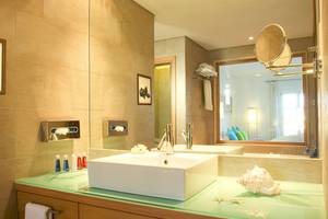Badezimmer im Petasos Beach Resort & Spa mit weißem Waschbecken und grünem Glastisch.